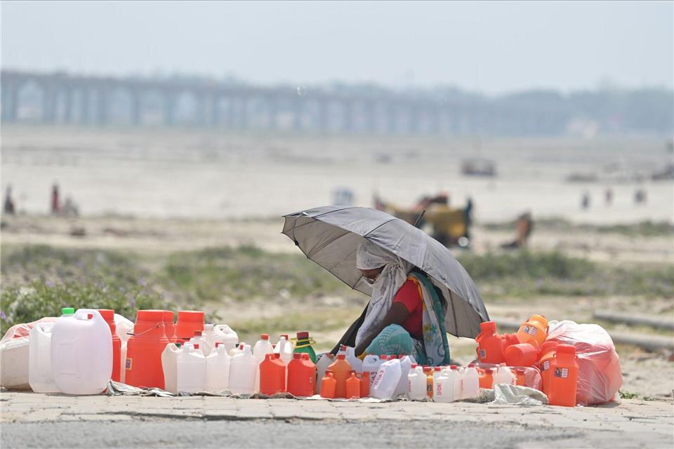 Von Kanistern umgeben wartet ein Verkäufer mit einem Schirm in Prayagraj auf Kunden.Prabhat Kumar Verma/ZUMA Press Wire/dpa