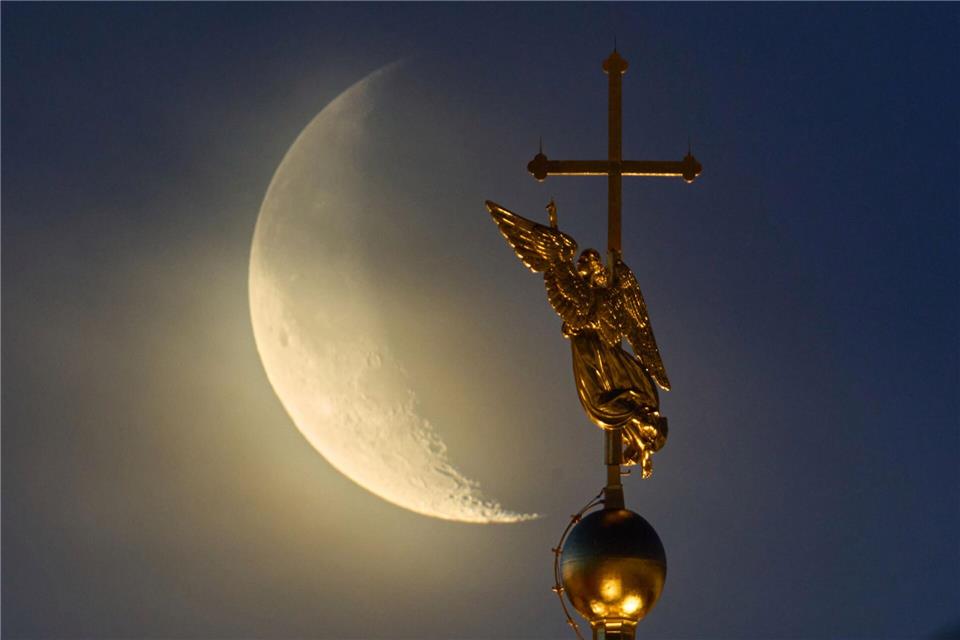 Vor dem Mond ist das Wahrzeichen der Stadt St. Petersburg, eine Wetterfahne in Form eines Engels, zu sehen.Dmitri Lovetsky/AP/dpa