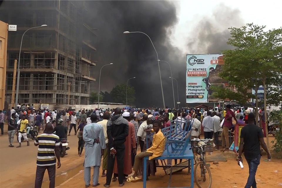 Vor der Kulisse des brennenden Hauptquartiers der Regierungspartei demonstrieren Anhänger meuternder Soldaten in Niamey.