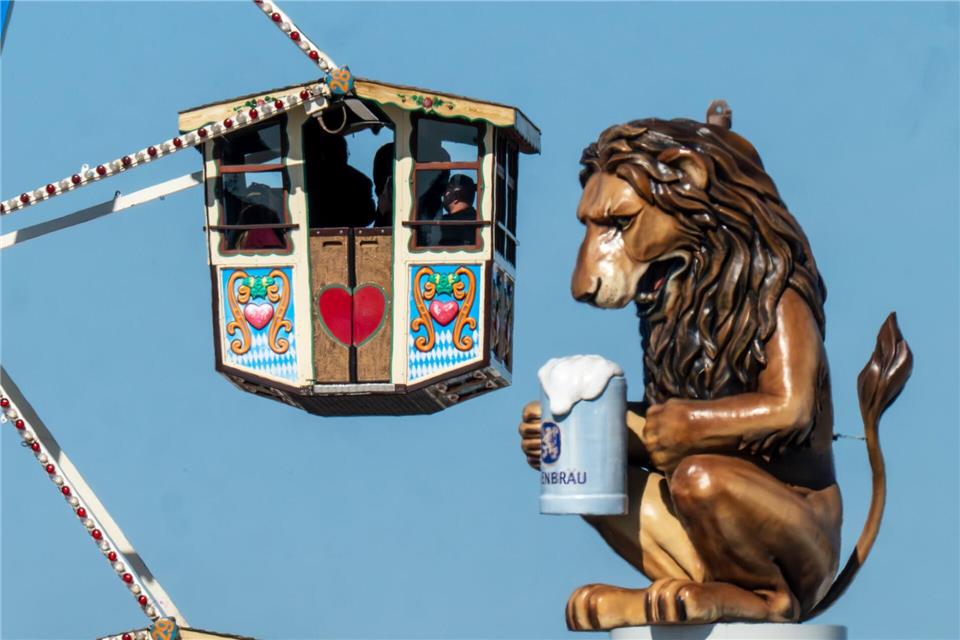 Wiesn-Besucher fahren in einem Riesenrad auf dem 190. Münchner Oktoberfest an der Kulisse einen überdimensionalen Löwen mit Bierkrugs vorbei.Peter Kneffel/dpa
