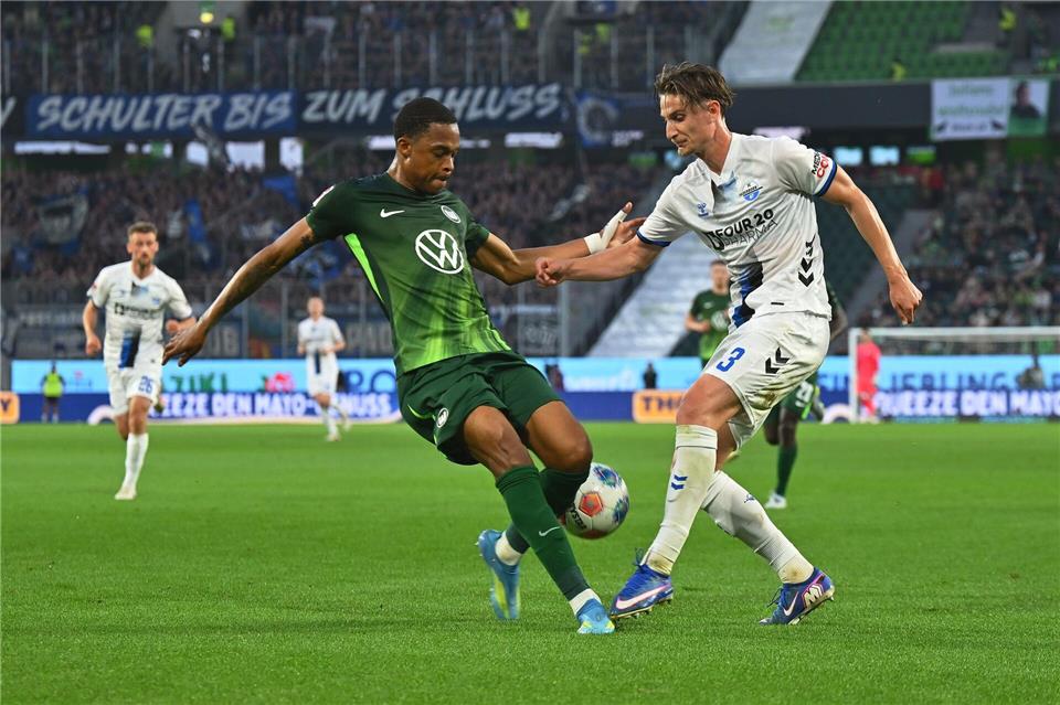 Wolfsburgs Jeanuël Belocian (l) stoppt den Paderborner Jonah Sticker. Swen Pförtner/dpa