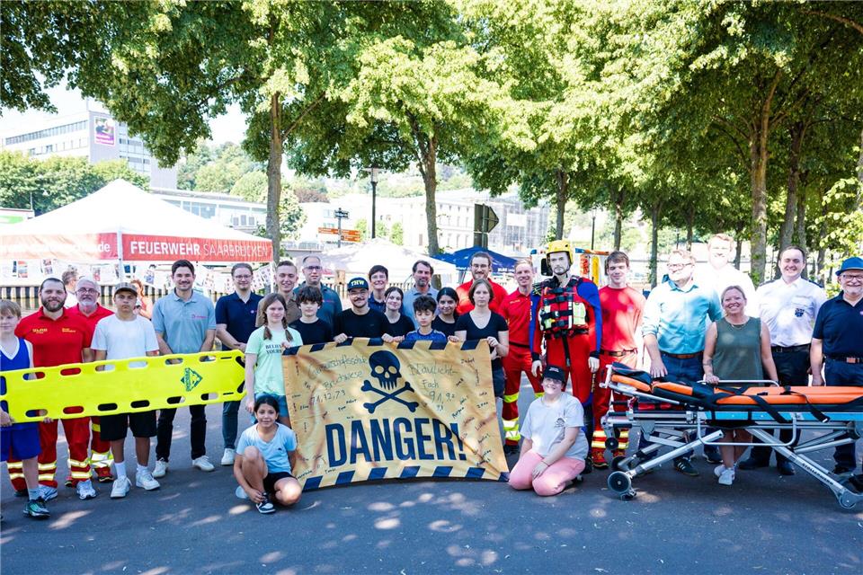 Zum Abschluss des Wasserrettungstags an der Saar versammeln sich Schülerinnen und Schüler der Klassenstufen 7 und 9 gemeinsam mit Vertretern von DLRG, Johannitern, Berufsfeuerwehr, Politik und weiteren Partnern zum Gruppenfoto.Laszlo Pinter/dpa