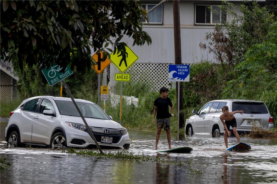Zwei Jugendliche surfen in Waialua neben einem liegengebliebenen Fahrzeug im Hochwasser.Stephen Lam/San Francisco Chronicle via AP/dpa