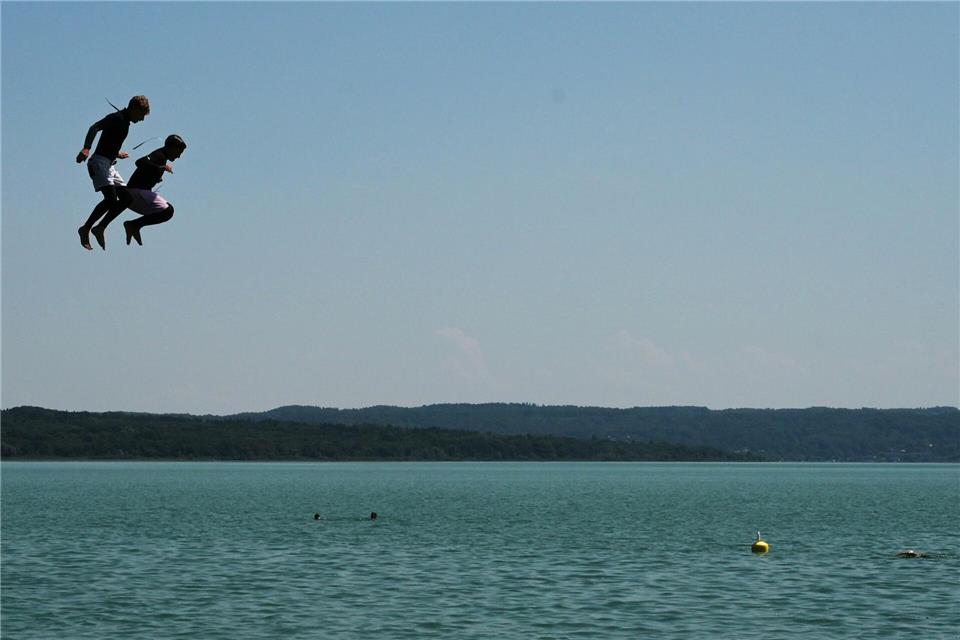 Zwei Jungen in Neoprenanzügen springen vom Sprungturm im Strandbad am Ammersee.Malin Wunderlich/dpa