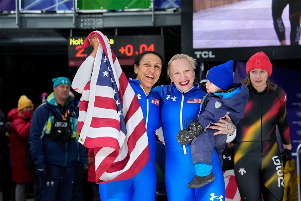 Zwei Mütter, zwei Medaillen: Monobob-Olympiasiegerin Elana Meyers Taylor (l) und die Bronzemedaillengewinnerin Kaillie Armbruster Humphries (2.v.l., mit ihrem Sohn Aulden im Arm) feiern im Ziel.Alessandra Tarantino/AP/dpa